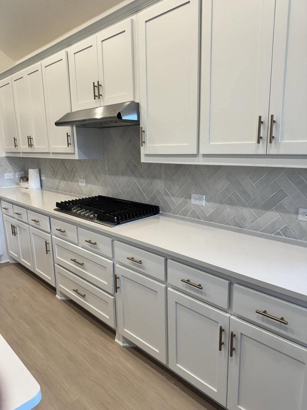 White kitchen cabinets with bronze pulls and herringbone backsplash